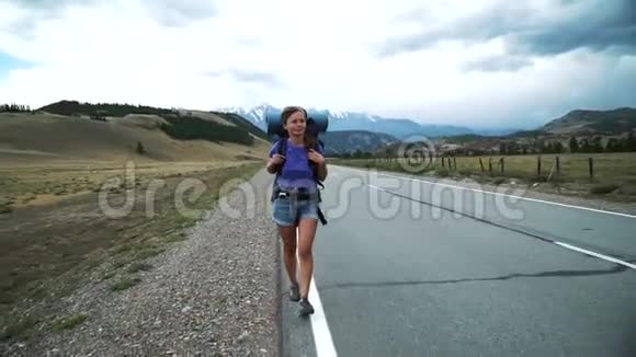 年轻的旅游妇女带着背包在山路上搭便车视频的预览图