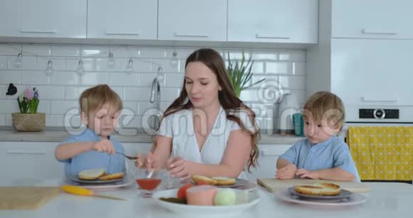 妈妈和两个孩子在厨房的餐桌上准备午餐汉堡视频的预览图