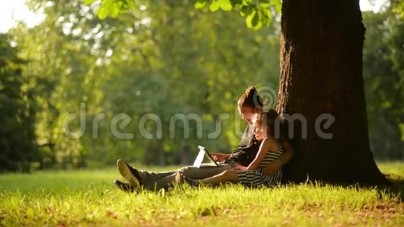 两个女孩在美丽的公园里用平板电脑一个温暖的夏日视频的预览图
