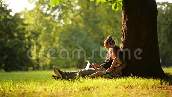 年轻的母亲和女儿在美丽的公园里玩平板电脑和狗视频的预览图