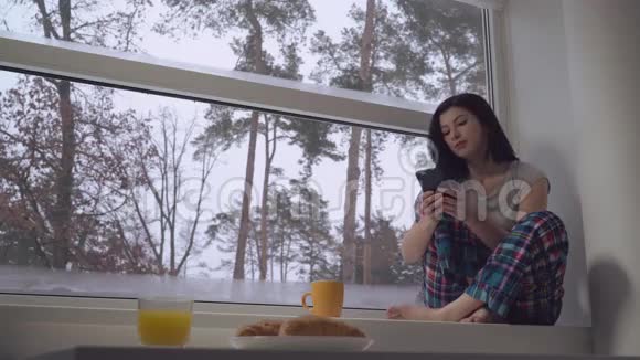 女性手持手机坐在窗台上视频的预览图