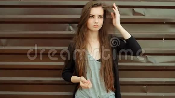 年轻美丽的白种人棕色头发的女人在城市的户外摆姿势望着远处沉思地靠在棕色的墙上视频的预览图