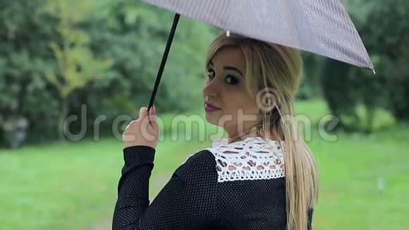 雨中带着雨伞的女人向公园里的照相机摆姿势穿着黑色礼服带伞的女孩视频的预览图