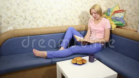 金发女孩坐在沙发上读一本书喝一杯自制的咖啡视频的预览图