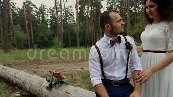 夏天森林里的时髦情侣一个年轻的女人站在她的爱人身边一个男人坐在一棵老掉下来的树上摄像机的动作视频的预览图