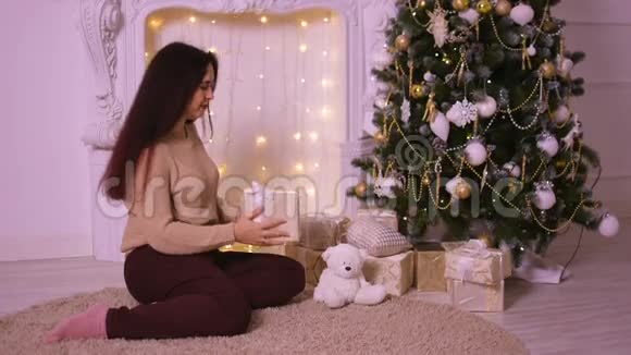 圣诞节壁炉旁美丽的年轻女子把礼物放在树下送给她的爱人视频的预览图