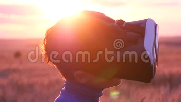 日落时分一个男孩戴着虚拟眼镜站在麦田里视频的预览图