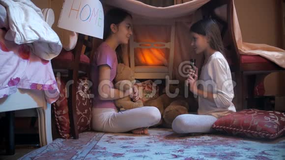 两个姐妹坐在卧室的毯子下面用手电筒讲故事视频的预览图