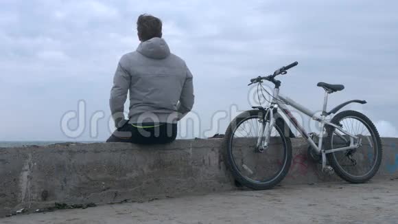 一个骑自行车的人在大风暴中坐在旧的高混凝土码头上视频的预览图