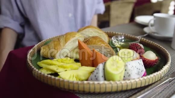 妇女早餐吃热带水果牛角面包薄饼和蜂蜜视频的预览图