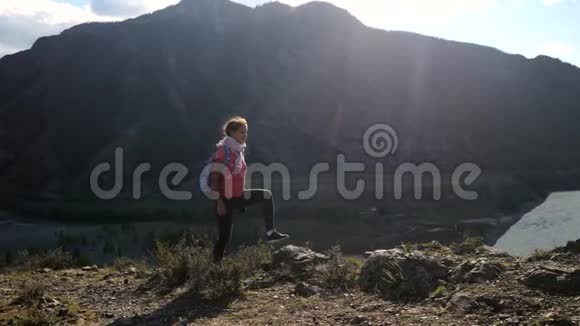 年轻的女徒步旅行者在山顶悬崖上用智能手机拍摄带有太阳耀斑效果的照片3840x2160视频的预览图