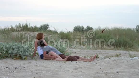 一对恋爱中的年轻夫妇在日落时躺在一个狂野的海滩上拥抱视频的预览图