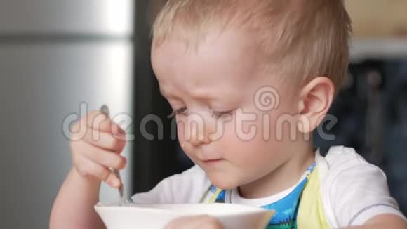 一个可爱的金发男孩用勺子从房子的盘子里吃粥特写视频的预览图