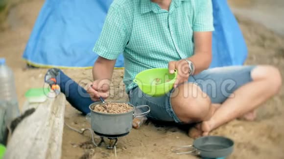 一个男人在营地里围着一个水壶吃饭背景是一个帐篷视频的预览图