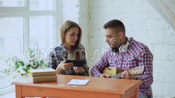 年轻快乐有爱心的一对夫妇学习用平板电脑弹声吉他坐在那里玩得开心视频的预览图