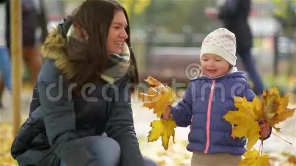 快乐的年轻妈妈和她的小女儿在秋天的公园里玩妈妈和女孩扔树叶和笑视频的预览图