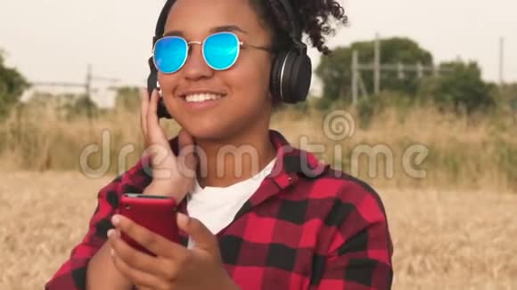 非洲裔美国少女少女蓝墨镜听音乐手机和无线耳机视频的预览图