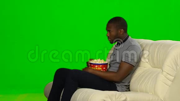 皮肤黑的男人看电视吃爆米花绿色屏幕视频的预览图