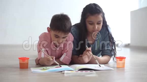 小男孩和小女孩在躺在地板上的相册上画着颜料视频的预览图