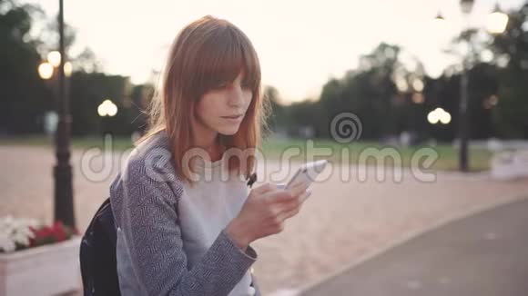 迷人的年轻红发女子在日落时分在公园里使用手机视频的预览图