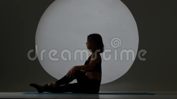 女人坐在瑜伽垫上伸腿背光剪影视频的预览图