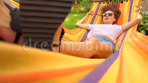 戴太阳镜的快乐黑发女孩在明亮的吊床上摇摆4K视频视频的预览图