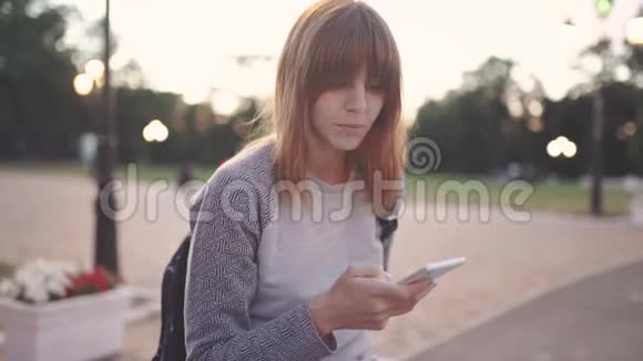 迷人的年轻红发女子在日落时分在公园里使用手机视频的预览图