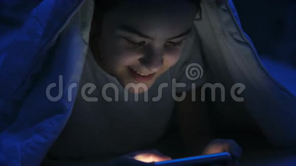 微笑少女躺在毛毯下的智能手机画像视频的预览图