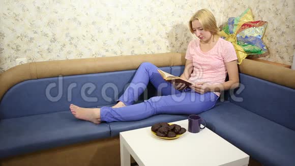 小姑娘坐在沙发上看书喝茶吃巧克力棉花糖视频的预览图
