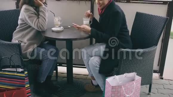 性感混血女人坐在街边咖啡馆的桌子旁一边说着手机一边她的朋友在冲浪视频的预览图