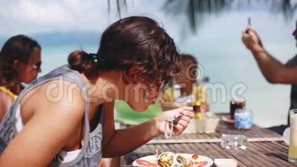 快乐的大家庭坐在海滩咖啡馆吃晚饭戴墨镜的女人吃泰国菜男人拍照视频的预览图