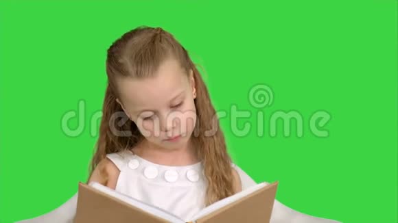 一个漂亮的小女孩坐在绿色的屏幕上看书Chroma键视频的预览图