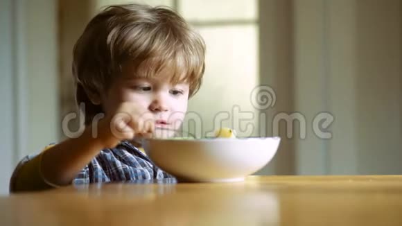 厨房里的孩子在桌子旁吃饭小男孩在厨房吃早餐快乐的小男孩勺子吃吃视频的预览图