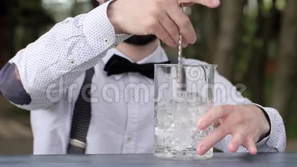 酒吧服务员在柜台上搅拌冰棒勺子玻璃上加冰特写酒保将饮料冷却到新鲜空气中视频的预览图
