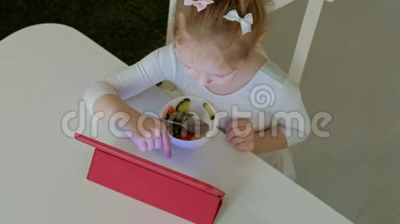 小女孩吃和玩电脑平板电脑网上冲浪视频的预览图