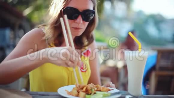 年轻优雅的幸福女人戴着太阳镜吃垫泰国炒面加鸡蛋泰国菜坐在咖啡馆里视频的预览图