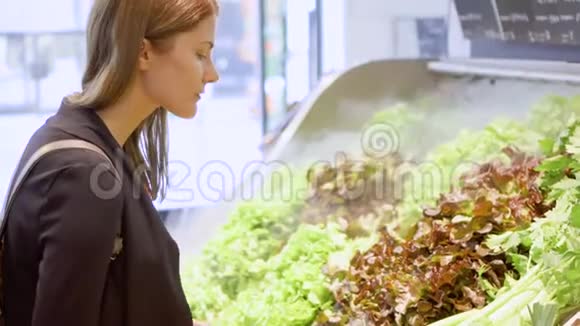 年轻女子在杂货店购物站在蔬菜部门选择新鲜的绿色沙拉视频的预览图
