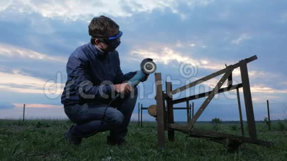一个年轻人在日落时打磨一台金属角磨机工人后面美丽的天空视频的预览图