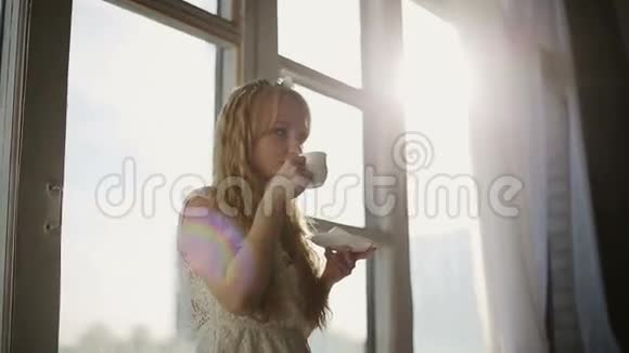 日出时在窗前喝咖啡的女人在她舒适的家视频的预览图