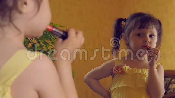 小女孩画她的嘴唇对着镜子涂口红的孩子穿着黄色裙子的漂亮小女孩正在看视频的预览图