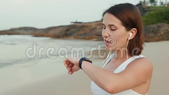 活跃的生活方式女性看科技智能手表特写宏观特写手臂海滩触摸屏手腕带视频的预览图