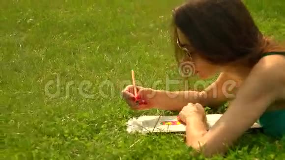 美丽的黑发女孩戴着太阳镜躺在草地上着色4K针色彩鲜明视频的预览图
