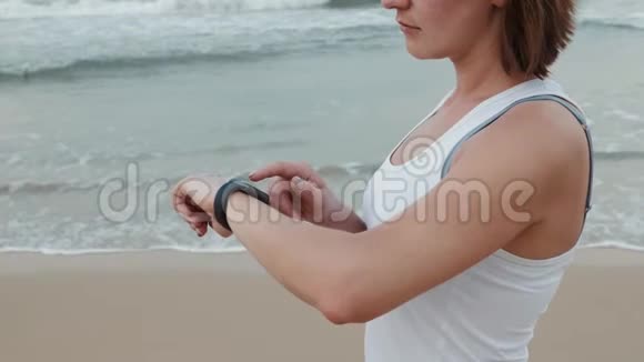 活跃的生活方式女性看科技智能手表特写宏观特写手臂海滩触摸屏手腕带视频的预览图