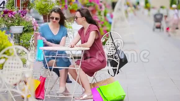 两位时尚的五颜六色的购物者带着袋子在露天咖啡馆购物售消费主义和人的观念高加索女孩视频的预览图
