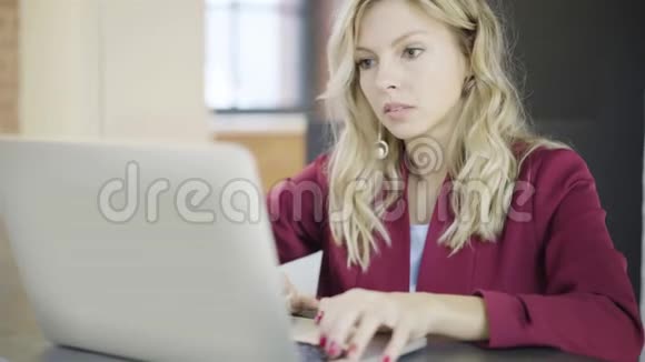 一位年轻漂亮的金发女商人在上班时打手提电脑视频的预览图