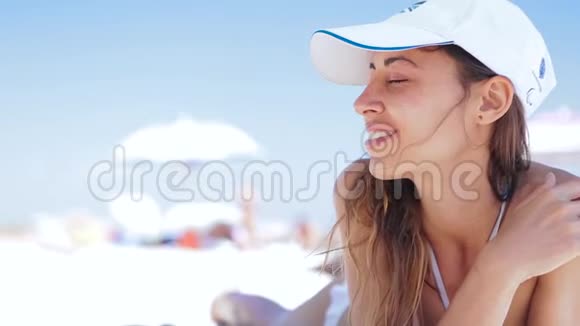 美丽的晒黑微笑的女人躺在沙滩上躺在沙滩上一边放松一边听着电话里的音乐视频的预览图