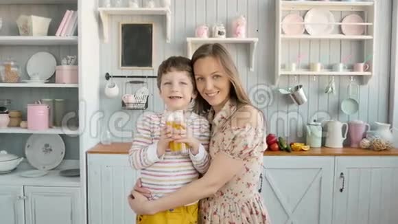 有趣的是三岁的孩子和母亲带着米色围裙在厨房里团队合作喝果汁吃水果视频的预览图