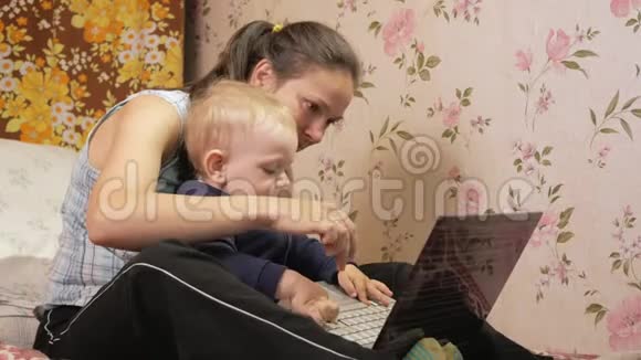 年轻女子带着儿子坐在家里的沙发上拿着笔记本电脑仔细看屏幕按下键视频的预览图
