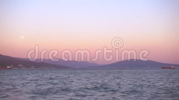 美丽的夕阳和月亮越过港口城市船在远处视频的预览图