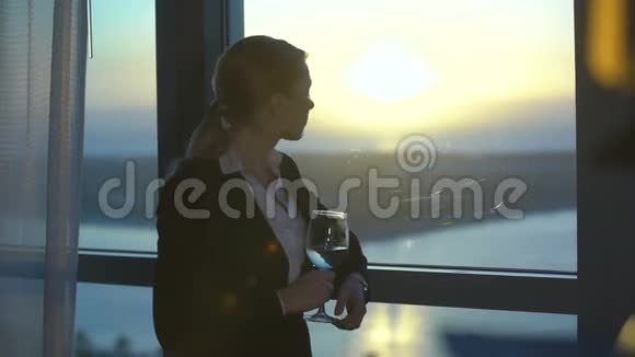 美丽的金发年轻商务女性在办公室酒店房间喝酒看日落视频的预览图